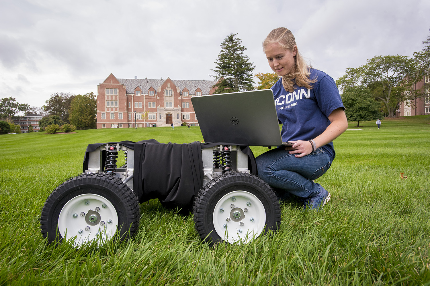 UConn student looking at the monitor of a robot on wheels